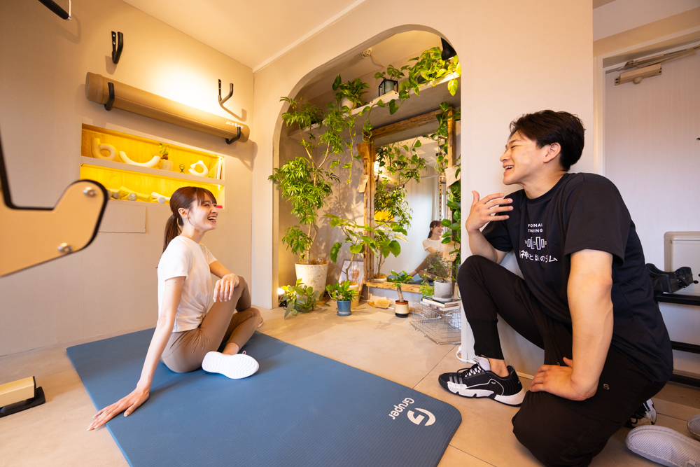 精神と時のジム二子玉川店でトレーナーと会話する女性